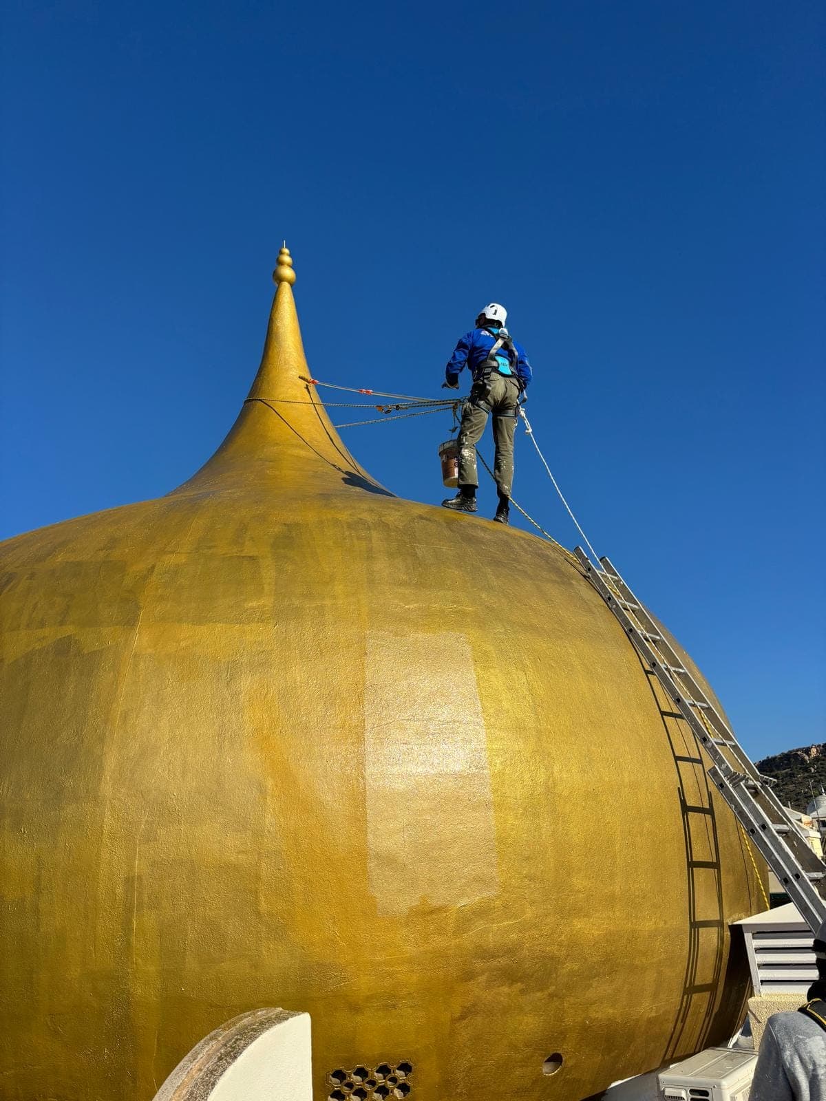 Técnico de Quarzo trabajando desde cuerda sobre una cúpula dorada, sin andamio